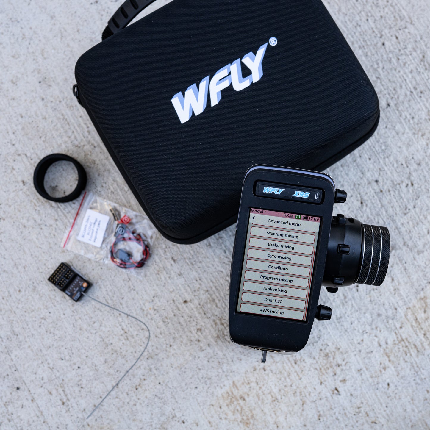 WFLY X9S RC transmitter with touchscreen interface showing advanced menu, displayed next to carrying case and included receiver