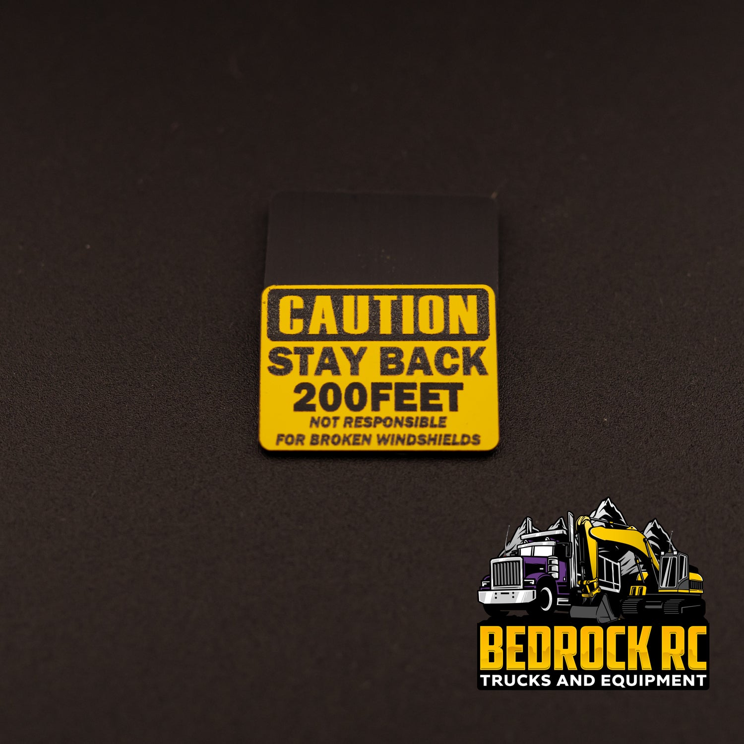 Bedrock Built Caution – Stay Back 200 Feet – Not Responsible for Broken Windshields sign for 1/14 scale RC trucks, laser-etched hard plastic, 31.5mm x 23mm, made in-house by Bedrock RC